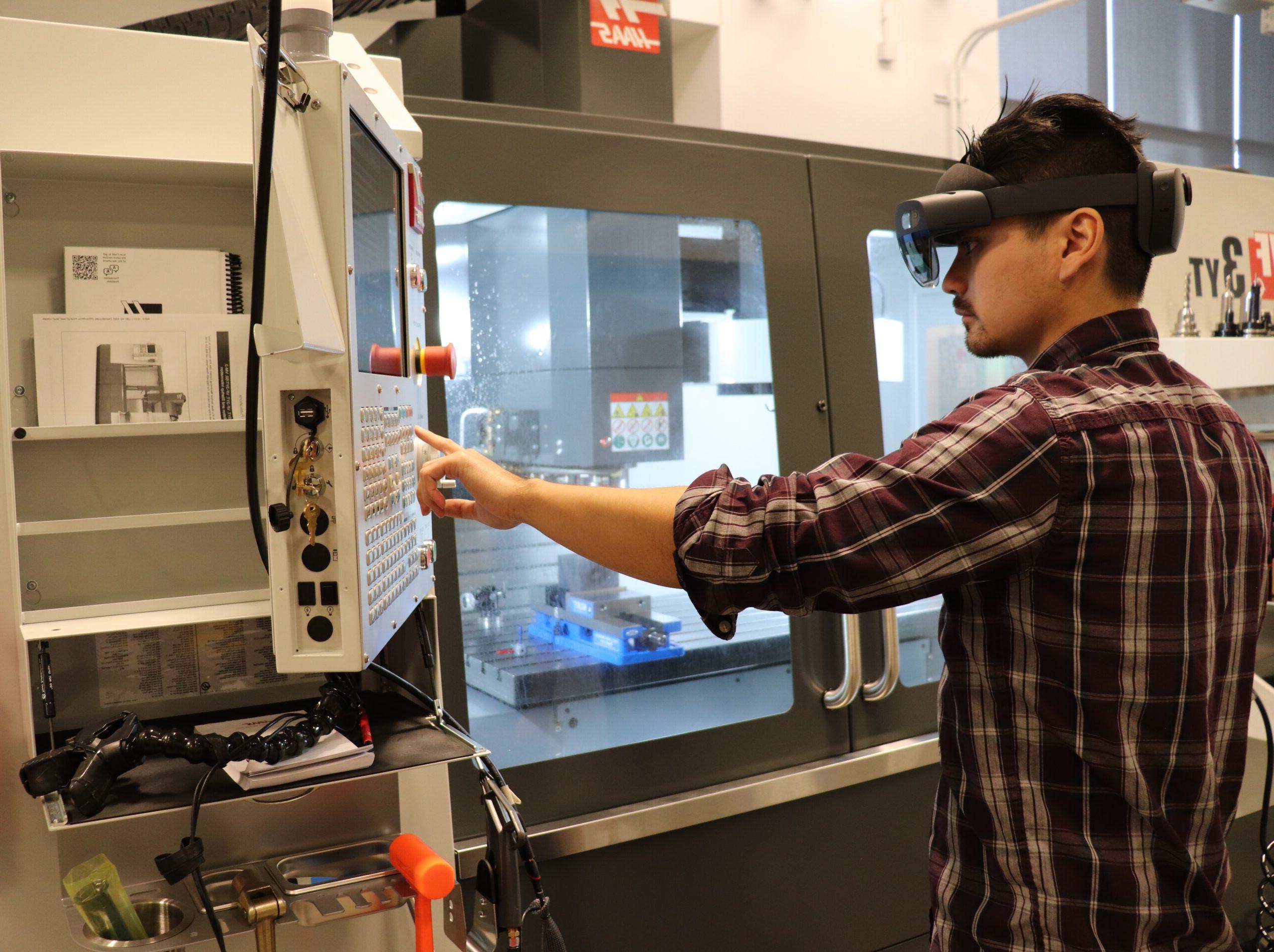 Student wearing augmented reality goggles pressing button on CNC machine